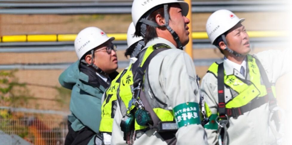 現場で上を見上げて確認するヘルメット姿の作業員